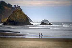 Two people walking on a beach near large rock formations and cliffs