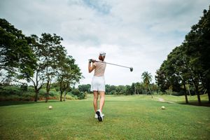 Golfer swinging on a golf course, trees in the background