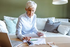 Older woman calculating finances using a smartphone and documents at a desk