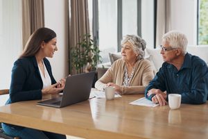 A woman conversing with an elderly couple at a table with a laptop