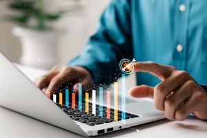 A person using a laptop while analyzing a digital graph with colorful bars and data points