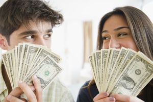 Man and woman holding U.S. dollar bills, smiling and looking at each other