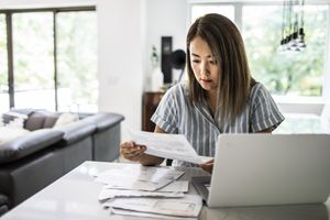 Person at a table reviewing documents with a laptop in a home setting