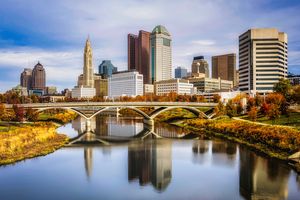 City skyline with a river and bridge in the foreground, showing urban buildings and reflections in the water