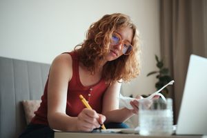 Young woman calculating spendings looking at bills making notes using calculator. 