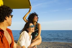 Three friends on a beach with one holding up an item and others smiling ocean background