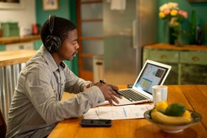 Man wearing headphones working on a laptop at a table in a home setting