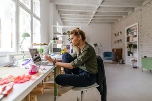 Person working on a laptop at a table in a spacious whitewalled room