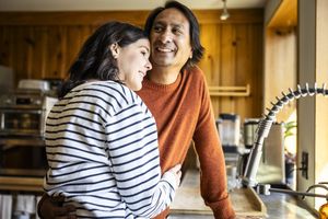 Two individuals standing in a cozy kitchen, one leaning on the countertop, close interaction and smiling