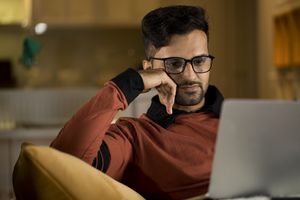 A man in glasses sitting on a couch using a laptop