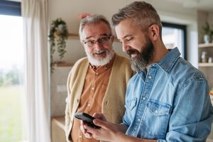 Two men one holding a smartphone standing indoors and sharing a moment