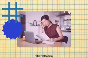 A person sits at a table reading printed materials and working on a laptop