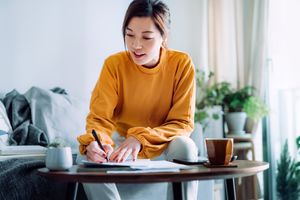 Person sitting and writing on a notebook placed on a coffee table