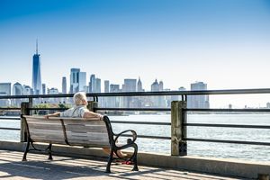 A person sitting on a bench looking at the New York City skyline across the water