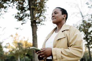 A person standing outdoors holding a smartphone trees in the background