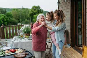 A woman and her child sharing a moment with an elderly woman on a wooden patio close to an outdoor table and a grill setup