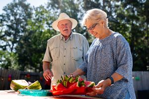 Two seniors in an outdoor setting one holding a platter of watermelon slices