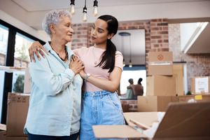 Two women in a supportive embrace standing in a room with boxes appearing to be engaged in moving or organizing tasks
