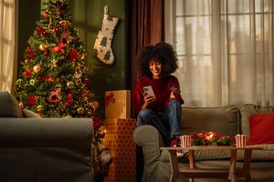 A young woman looks at her phone next to a Christmas tree
