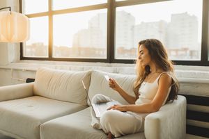 A woman seated on a couch holding a card and using a laptop