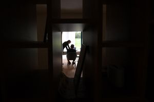 A caregiver is seen through a hallways speaking with an older adult patient.