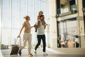 Family with luggage walking in an airport terminal father carrying child on shoulders mother pulling suitcase