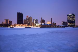City skyline with illuminated buildings at twilight seen across a frozen body of water