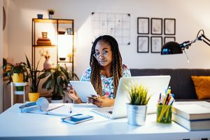 Young millennial makes a budget on tablet and laptop at home.