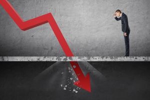 Businessman looking down at the falling red arrow destroying a concrete barrier.