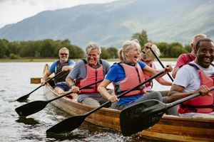 Group of people paddling on a large canoe smiling and enjoying recreation on water