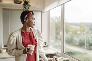 A person holding a mug looking out the window in a cozy home setting