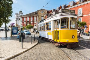 Yellow tram on a street in Lisbon Portugal with surrounding urban architecture and parked cars