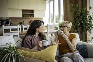 Two people sitting on a couch holding mugs surrounded by moving boxes and houseplants