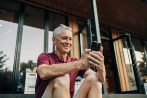 Man smiling and using a smartphone while seated outdoors