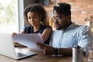 Two young people looking intently at documents with a laptop open.