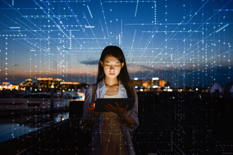 Woman using a device with a futuristic digital display overlay outdoors at night