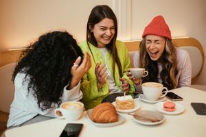 Three people laughing together at a table with coffee cups and pastries