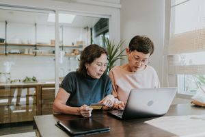 Two people sitting at a table one holding a credit card the other looking at a laptop screen