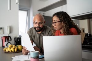 A couple reviewing documents together in their kitchen a laptop and fruit bowl visible on the table