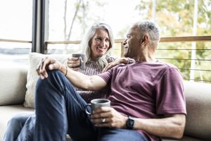 Two people sitting on a couch holding mugs smiling at each other