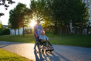 A caregiver pushing a person in a wheelchair along a pathway at sunset