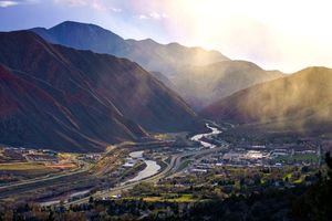 A valley with a river roads and buildings framed by mountains at sunset mist in the air