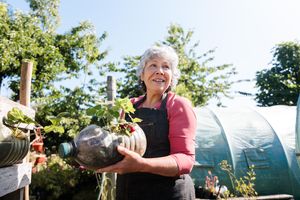 A person in an outdoor garden setting holding a plant in a recycled container