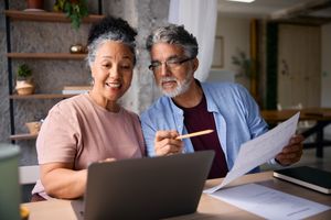 An older couple working together at a laptop reviewing documents and discussing