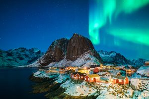 Northern lights over a snowy village with mountain and water in the background