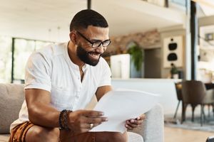 A man sitting on a sofa reading a document and smiling