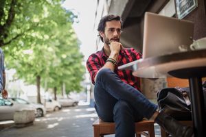 Man seated outdoors working on a laptop at a cafe table