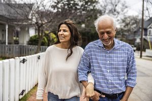 A couple walking together on a neighborhood street smiling and holding each others arms