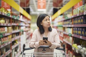Woman in her 30s pushing her cart down the grocery aisle with look of concern