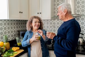 Two people enjoying drinks in a kitchen surrounded by fresh fruits and a blender